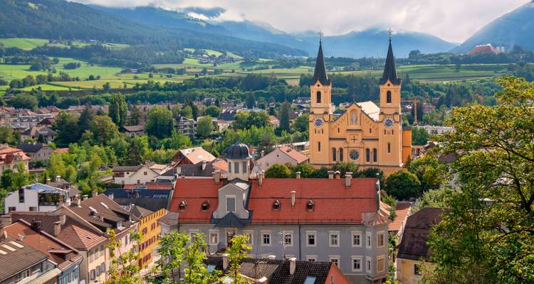 Malerische Stadt mit einer markanten Kirche, umgeben von üppigem Grün und Bergen.