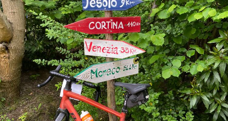Panneau de signalisation avec des distances vers plusieurs destinations, vélo appuyé contre celui-ci.