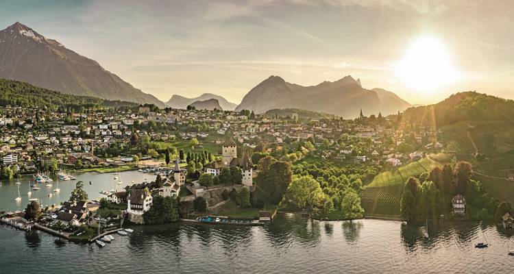 Coucher de soleil sur une ville au bord d'un lac avec des montagnes en arrière-plan.