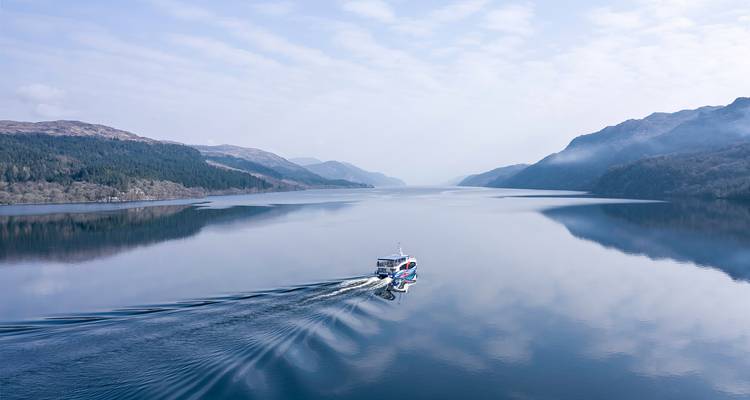 Boot varend op een serene meer omringd door bergen en bossen.