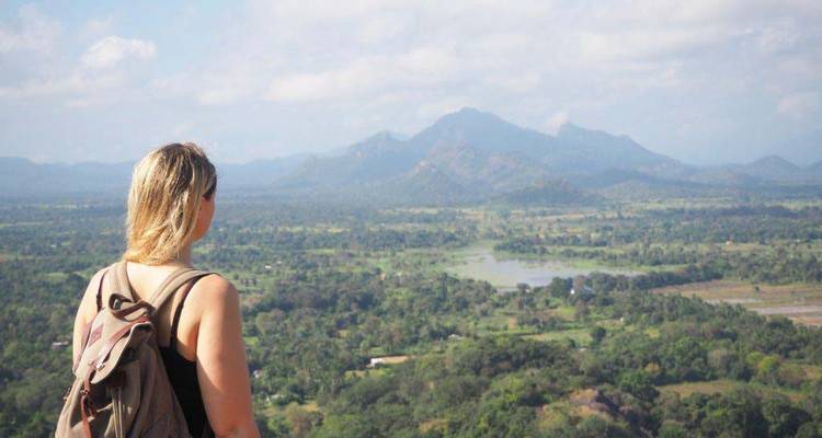 Personne avec un sac à dos contemplant un vaste paysage depuis un point élevé.