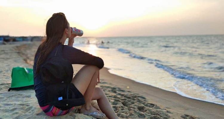 Personne assise sur une plage buvant dans une canette avec l'océan en arrière-plan.
