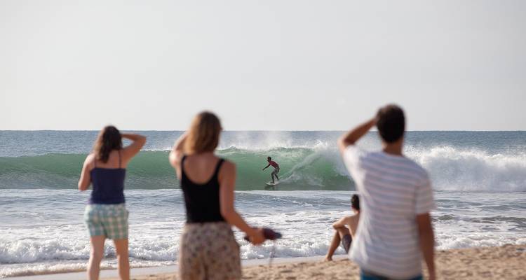 Surfeur chevauchant une vague, observé par des gens sur la plage.