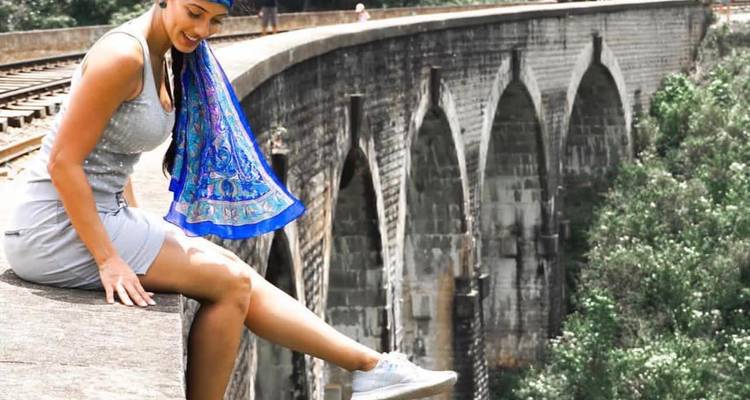 Femme assise sur le bord d'un pont en pierre, souriante.