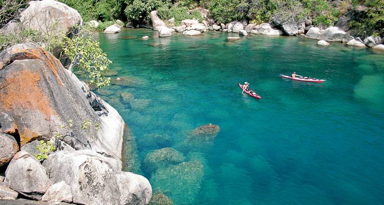 Kayakers in clear turquoise water surrounded by rocks and trees.