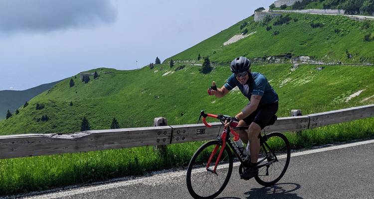 Cycliste faisant un pouce levé en roulant sur une route de montagne pittoresque.
