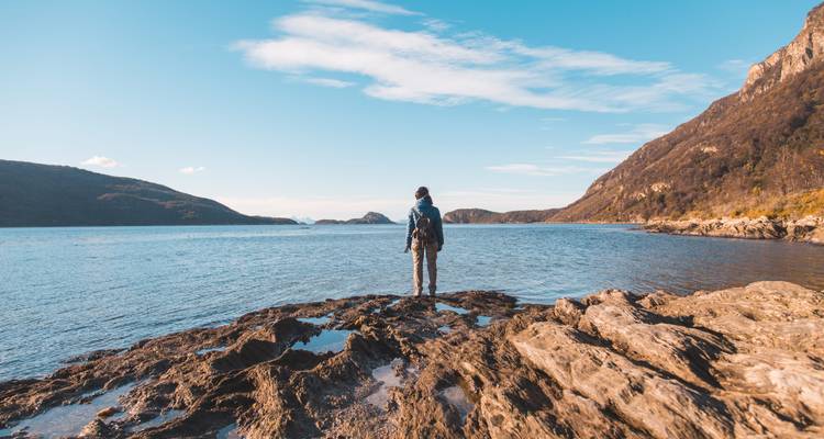 A person standing on rocks looking at a serene body of water.