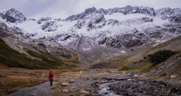 Randonneur en terrain montagneux avec des sommets enneigés.