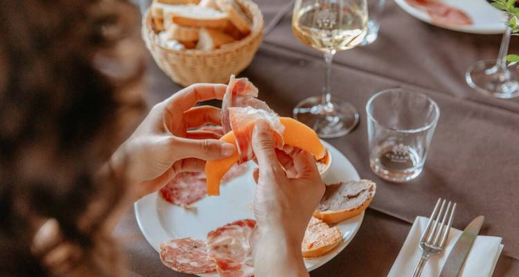 Personne épluchant des fruits à une table avec du vin et de la charcuterie.