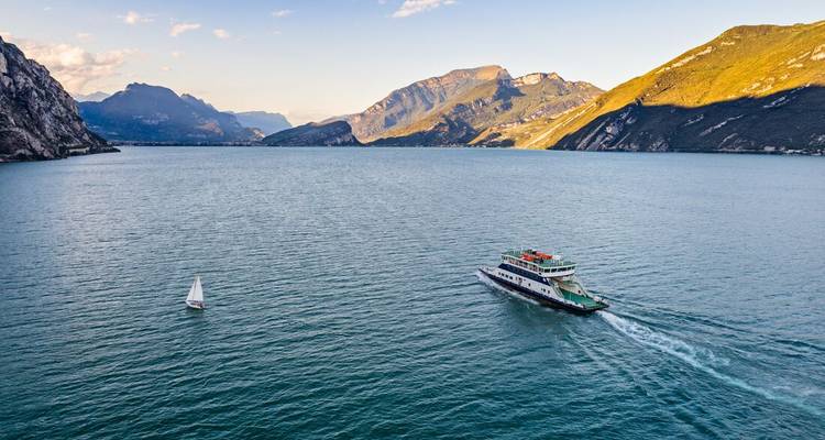Un ferry et un voilier sur les vastes eaux du lac de Garde avec des montagnes en arrière-plan.