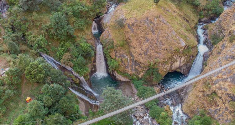 Pont suspendu traversant une rivière avec cascades et verdure.