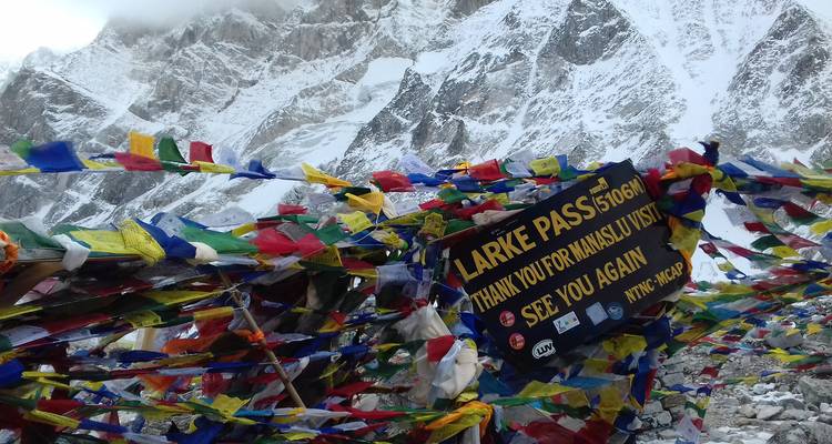 Panneau au col de Larke entouré de drapeaux de prière avec des montagnes en arrière-plan.