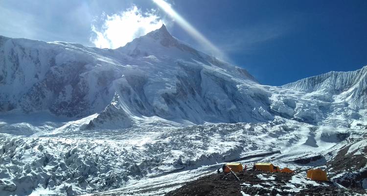Paysage de montagne enneigée avec des tentes au premier plan.