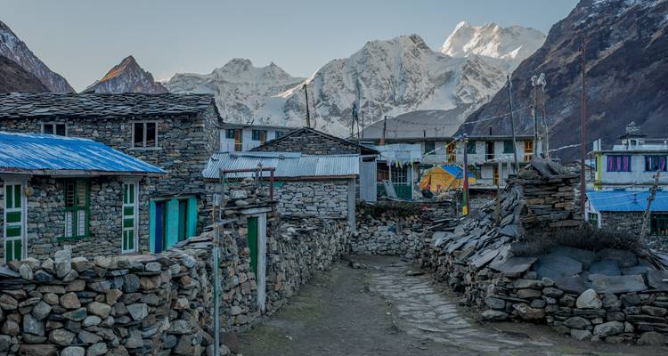 Village de montagne avec des maisons en pierre et des sommets enneigés en arrière-plan.