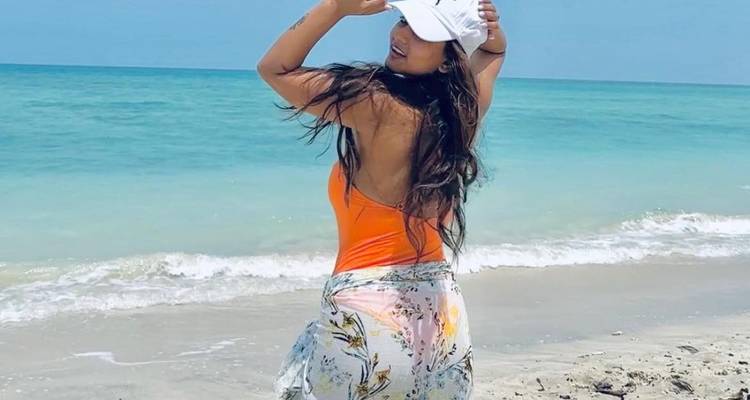 Femme posant sur une plage avec de l'eau turquoise.