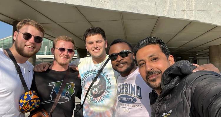 Amigos sonriendo para una selfie fuera de un edificio moderno en un día soleado.