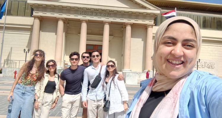 Selfie del grupo de viaje frente al Museo Nacional de Alejandría con columnas y banderas egipcias.