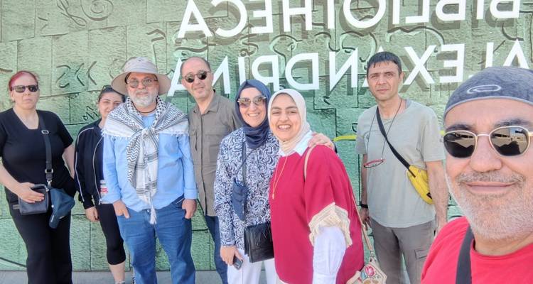 Grupo posando frente al muro espejado de la Bibliotheca Alexandrina con escritura grabada.