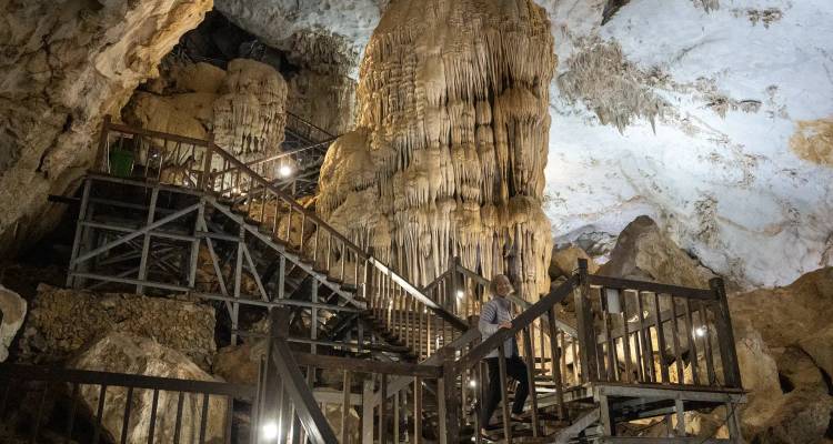 À l'intérieur d'une grotte avec une personne marchant sur des escaliers en bois, entourée de stalagmites et de stalactites.