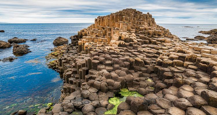 Basaltsäulen des Giant's Causeway, die in den Atlantik ragen, umgeben von leuchtend blauem Wasser
