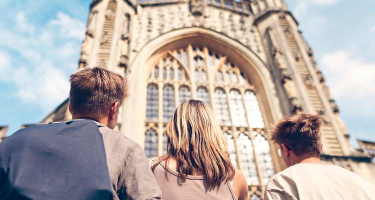 Tres jóvenes viajeros miran hacia arriba a una gran fachada de iglesia gótica desde el patio de abajo.