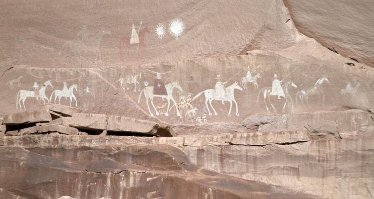 Rocky cliff face with petroglyphs depicting ancient figures and horses.