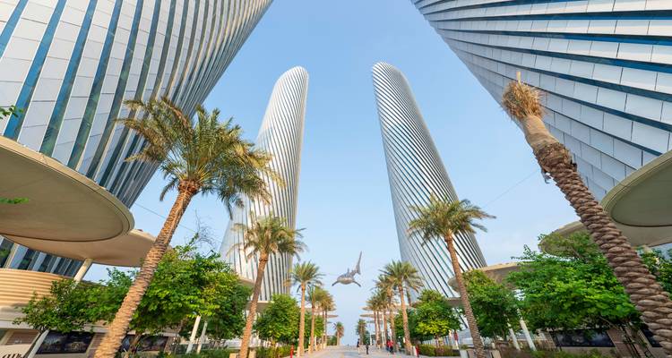 Modern architectural buildings with palm trees and clear sky.