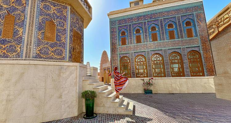 Person walking through a courtyard with ornate architectural buildings.