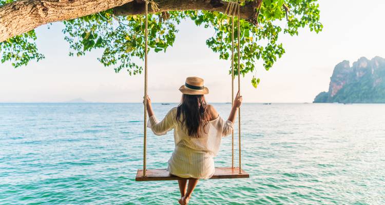 Femme sur une balançoire suspendue à un arbre, dominant l'océan.