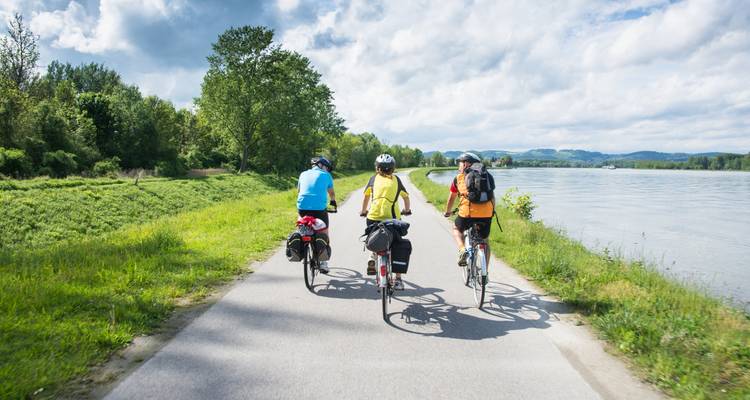 Three cyclists riding along a river path with scenic views.