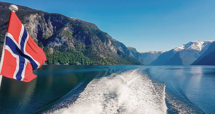 Blick auf einen norwegischen Fjord mit Bergen und einer sichtbaren Flagge.