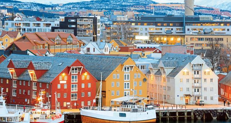 Edificios coloridos junto a un puerto con montañas cubiertas de nieve.