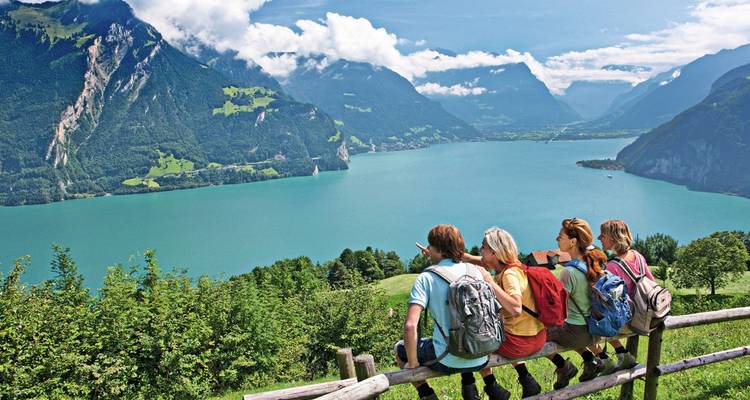 Eine Gruppe von Wanderern, die auf einem Zaun ruht und einen ruhigen See und Berge überblickt.
