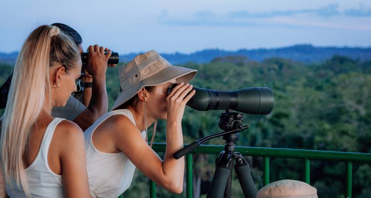 Des personnes utilisant des jumelles sur un balcon donnant sur une zone boisée.