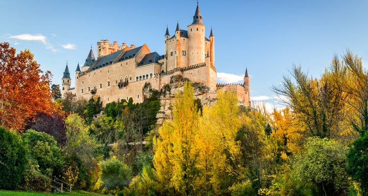Alcázar de Ségovie entouré de feuillage automnal coloré sous un ciel dégagé.