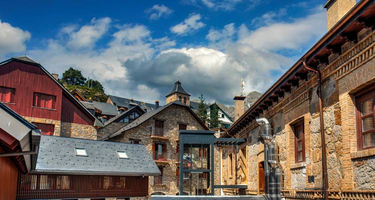 Ville de montagne avec des bâtiments traditionnels en pierre et un ciel nuageux.