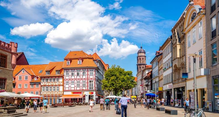 Street view of a busy square with half-timber houses and people.