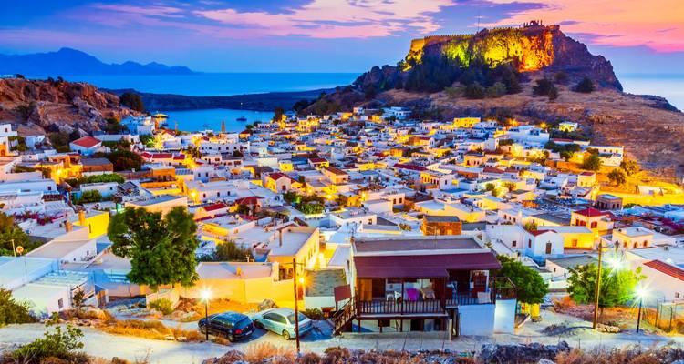 Coucher de soleil sur une ville au sommet d'une colline à Rhodes avec des bâtiments illuminés.