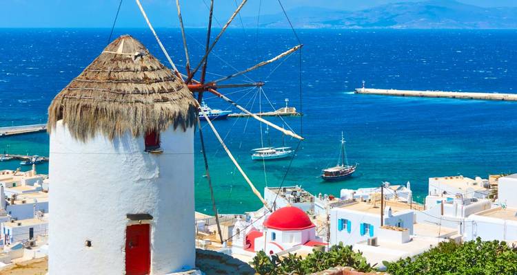 A white windmill overlooking the sea with boats.