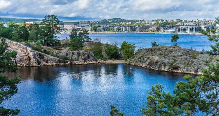Coastal scene with rocky shores and cityscape of Kristiansand in the distance.