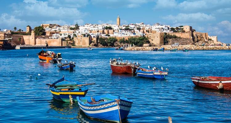 Bunte Ruderboote mit Möwen ruhen auf blauem Wasser gegenüber den ockerfarbenen Mauern von Rabats Kasbah und der weißen Medina.