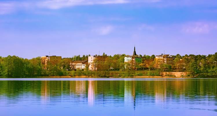 Buildings reflecting in a calm lake under a clear sky.