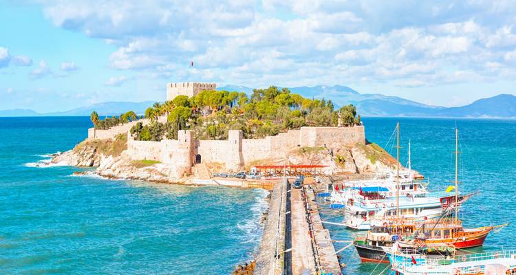 Castle on an island with a bustling harbor and blue waters.
