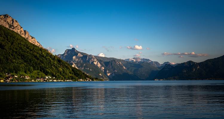 A scenic lake with surrounding mountains and villages under a dramatic sky.