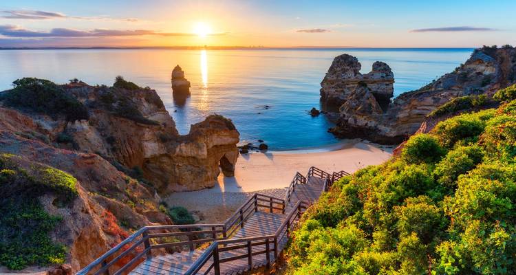 A scenic view of a beach at sunset with cliffs and ocean.