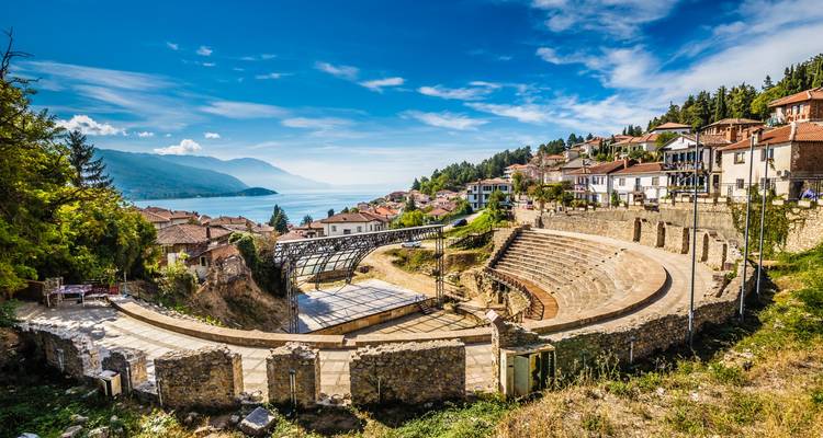 Amphithéâtre antique avec vue sur un lac et des montagnes au loin.
