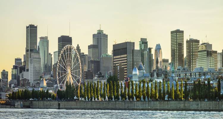 Montreal skyline at dawn with La Grande Roue Ferris wheel and modern towers reflected on the river.