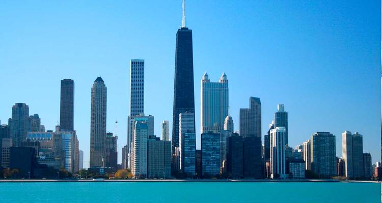 Chicago skyline seen across Lake Michigan featuring the tall black John Hancock Center on a clear day.