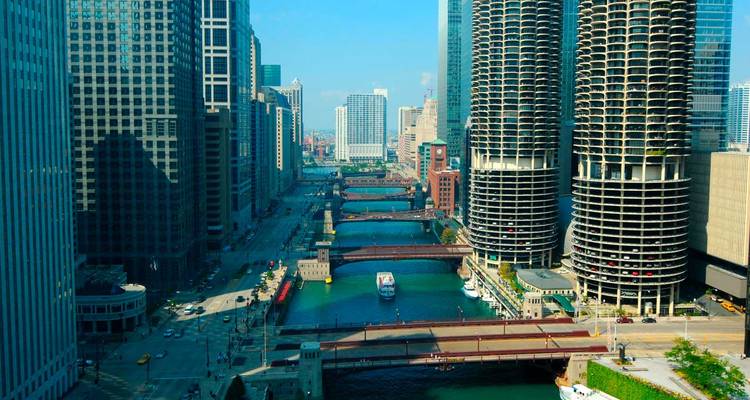 Chicago River canyon with tour boat passing under bridges between glass skyscrapers and Marina City towers.