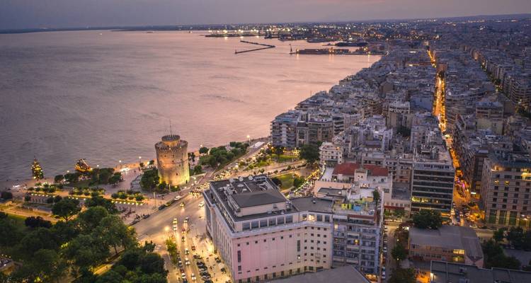 Vue aérienne nocturne d'une ville portuaire avec une tour historique proéminente et des rues bordées de lumières.